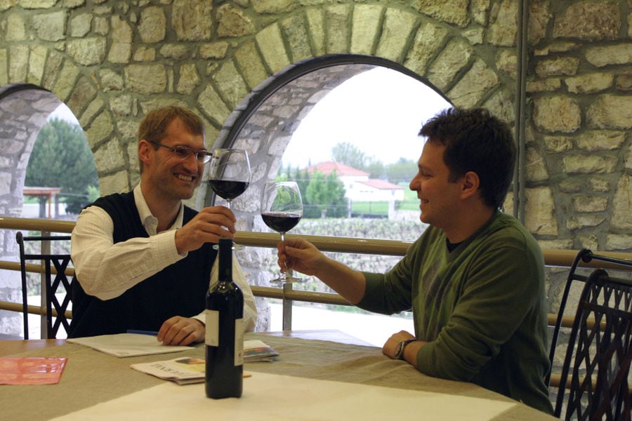 two men smiling happily and clink glasses for cheers at Ktima Spiropoulos winery